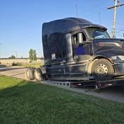 A BC Highway Patrol vehicle supervises as a black transport truck with no rear suspension is halfway up a flatbed loading ramp