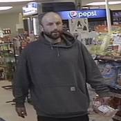 Unknown individual #2, a man with short brown balding hair, and a full beard. He is seen wearing a grey hoodie with a white label on the front pouch;
