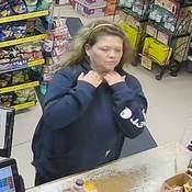 Unknown individual #3, a woman with long blond hair, a head band, and pierced ears. She is seen wearing a dark blue hoodie with white lettering on the left sleeve;