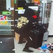 An individual with their back to the camera, is seen holding onto an item over a large garbage bin. The person is dressed all in black, and is seen wearing a black coat or hoodie with a large yellow logo on the back with the words “WORKING HARDER.”