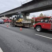 A tractor on a trailer is hooked up to a tow truck.