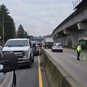 A police officer in a yellow jacket is in the middle of the highway with trucks lined up in both directions.