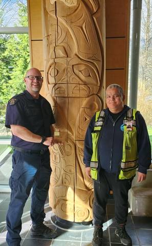 Integrated First Nations Policing RCMP Officer Cst. Dean handing a reward to the Good Samaritan Christopher Thomas standing in the Sea to Sky RCMP- Squamish lobby