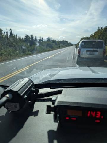 A grey minivan is pulled over on the side of a road. A police vehicle’s radar is pictured in the foreground displaying a speed of 143 km/h.