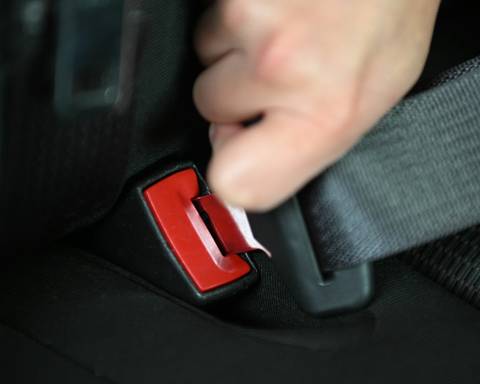 A hand buckling up their seatbelt in a car | Une main bouclant sa ceinture de sécurité dans une voiture.
