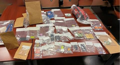 A number of items are displayed on a table, including quantities of drugs, cash, cell phones, tools and drug paraphernalia;