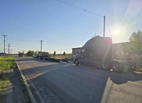 A black transport truck being loaded onto a flatbed while a tow-truck driver supervises