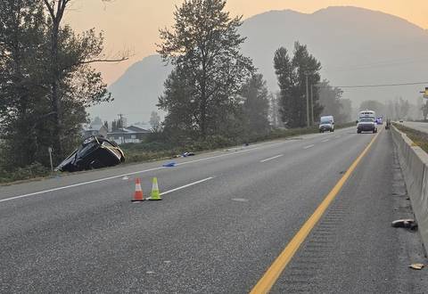 A black GMC Sierra pickup rolled over in a ditch off Highway #1 with police vehicles investigating in the background