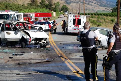 RCMP officers look over a wrecked white Ford Explorer and emergency vehicles on Highway #97 near Oliver