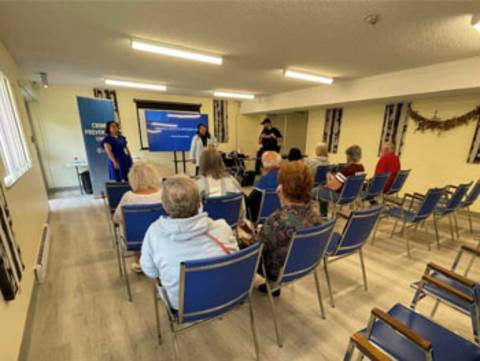 Three people, including a police officer, stand in front of a group of seniors while giving a presentation