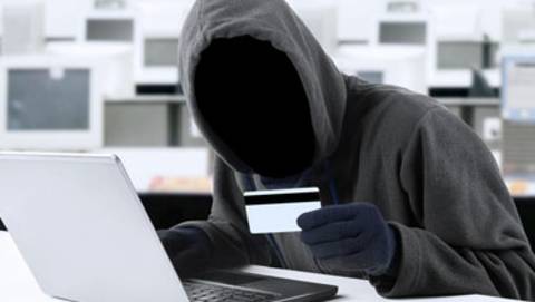 A faceless man at a computer, holding a card